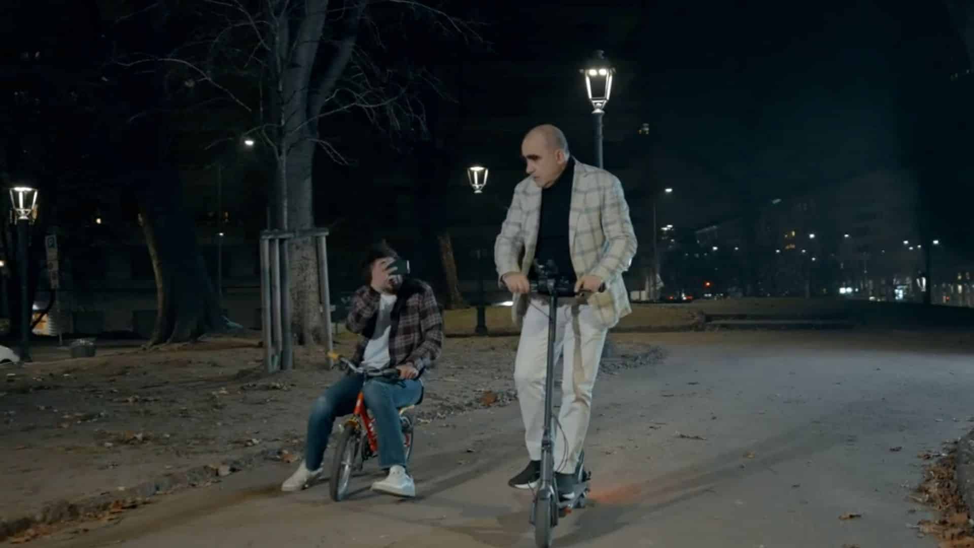a freeze frame from Plesh's immersive hybrid event - 2 Italian actors in a park at night time - one on a scooter, the other on a bike taking a picture with his phone