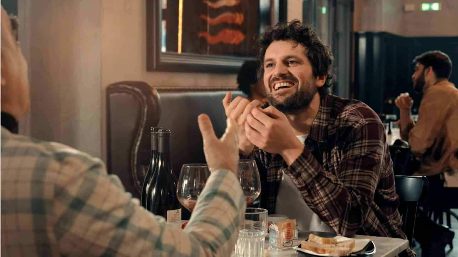 a freeze frame from Plesh's immersive hybrid event- an interactive video - a man laughs whilst in conversation to another man. Location - restaurant.