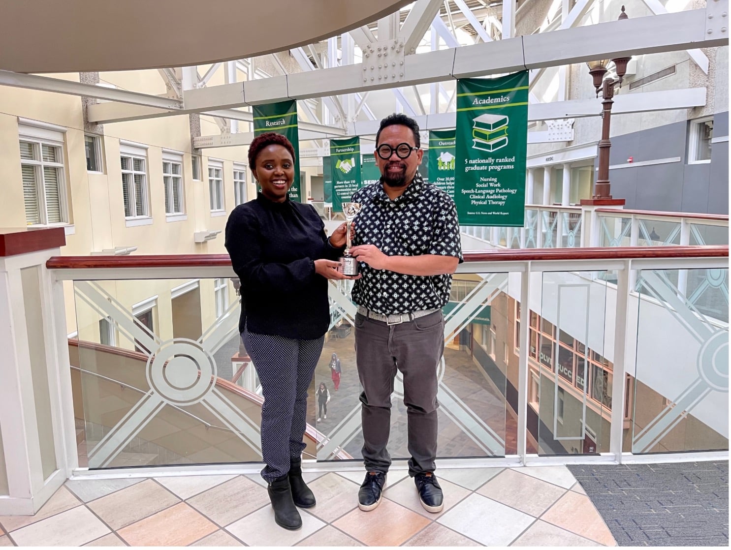 Kingori and Durado with the Davey Awards Plaque. DatingForward has so far won 2 award. 2 people stand in a university building holding an award.