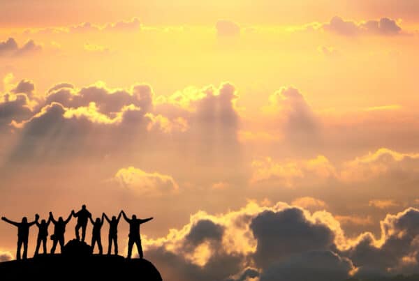 A group of happy people silhouetted on a mountain top looking at a sunset