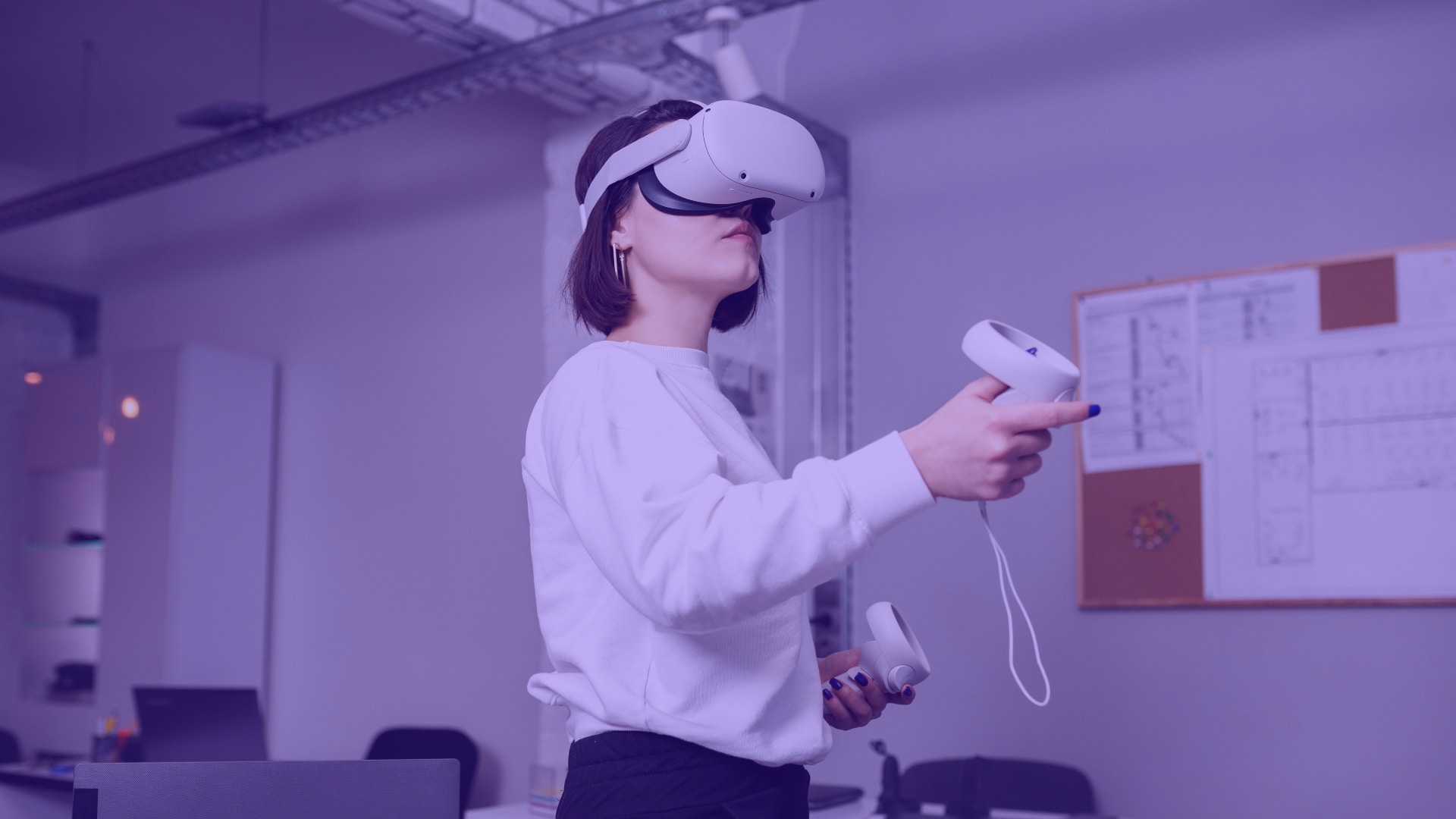Woman in meta quest VR headset - a women stands in an office in a VR headset. She holds controllers in her hands.