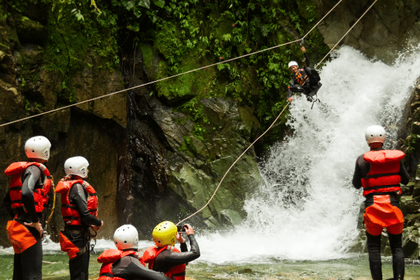Adaptive learning with adaptive video - people stand in a river wearing red helmets and safety gear as a person zip lines over a small waterfall